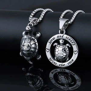 Detail of stainless steel turtle pendants with engraved motto on black reflective background
