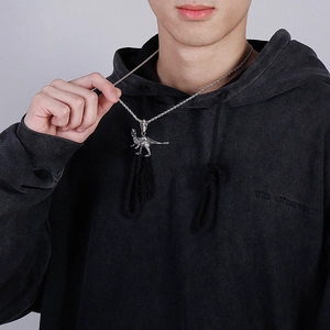 Detail of silver dinosaur pendant with twisted chain worn over a black hoodie garment