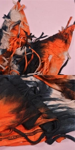Detailed view of tie-dye fringe tassel fabric on an orange and black mesh knit dress