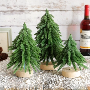 Three green flocked Christmas trees with wooden bases on snow-covered wooden surface