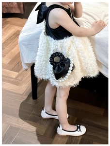 Detail of elegant black pleated kids handbag with pearl handle and golden chain strap