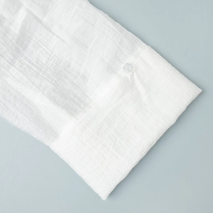 Dettaglio del polsino della camicia in lino bianco con bottone traslucido e cuciture fini