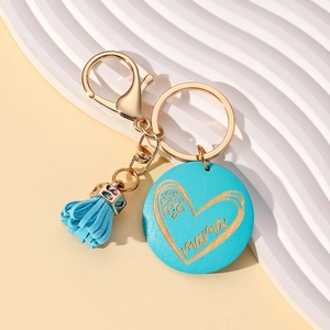 Detail of blue tassel keychain with engraved wooden mama charm and golden clasp on wave surface