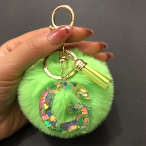 Detail of green faux fur pompom and resin letter G keychain with heart sequins