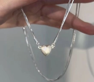 Detail shot of hand holding a silver heart pendant necklace with layered snake chain style