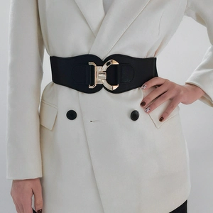 Detail of a black wide elastic waist belt with a gold geometric metal buckle on a white blazer