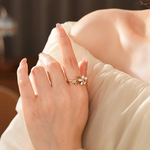Dettaglio dell'anello a fiore dorato con smalto bianco e pietre verdi a foglia