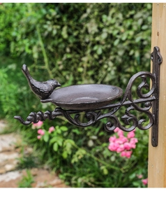Detail of vintage cast iron bird feeder with decorative scrollwork mounted on a wooden post