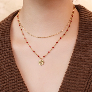 Close-up of double-layer golden chain necklace with red beads and flower charm