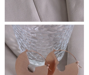 Close-up of rose gold textured hoop earrings with cutout design on glass background