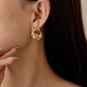 Close-up of golden irregular geometric textured earring worn by a model in soft light