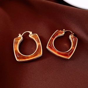 Close-up of 18k gold plated square resin earrings with amber texture on red silk fabric