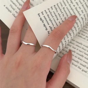 Detail of two minimalist wavy 925 silver rings worn on fingers over a book backdrop