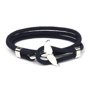 Detail of blue braided Milan rope bracelet featuring a polished silver whale tail anchor