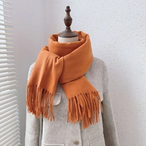 Elegant solid orange cashmere-like scarf with tassels styled on a cream-colored coat