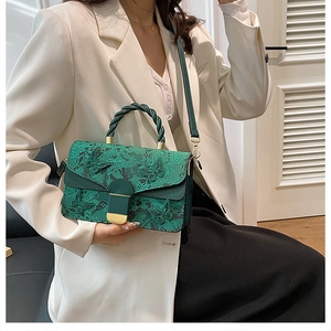 Close-up of green handbag with floral embroidery and unique woven handle on white blazer
