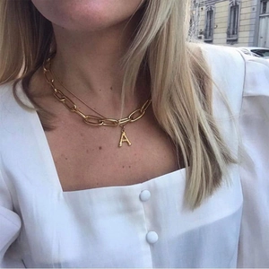 Detail of layered gold chunky chain and fine necklace with letter A pendant on a model