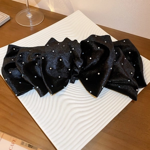 Détail d'une pince à cheveux nœud noir scintillant avec strass sur un plateau texturé