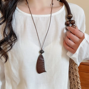 Detail of vintage wooden moon pendant on a brown cord worn with a linen outfit