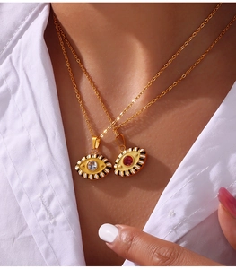 Macro detail of gold layered Evil Eye necklaces with blue and red stones on a white shirt