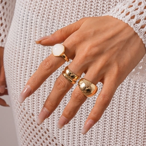 Detailed view of gold-tone geometric resin and metal rings set worn by a model