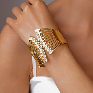 Detail eines goldenen Cut-Out-Armreifs mit vertikalen Strasssteinen am Handgelenk