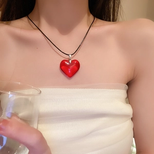Gros plan d'un collier avec pendentif cœur en verre rouge sur cordon noir porté par un mannequin
