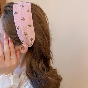 Détail d'un serre-tête en tissu rose avec étoiles dorées et rivets décoratifs