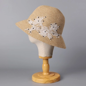 Detail of elegant straw hat with delicate white lace floral patches and black bead accents
