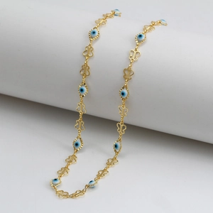 Detail of gold-plated evil eye beads and butterfly chain links on white pedestal
