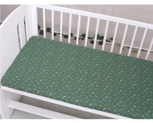 Green cotton baby fitted sheet with white animal patterns on a wooden crib