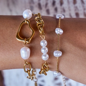 Detailed view of stacked gold titanium steel bracelets with heart charm and white pearls