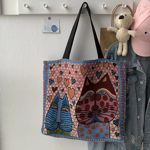 Detail of artistic woven tapestry tote bag featuring colorful cat and heart patterns