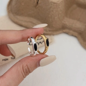 Detailed view of silver and gold rings with black oval inlays on a beige background