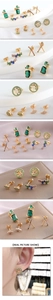 Macro view of gold plated earrings set featuring green zircons on white silk background