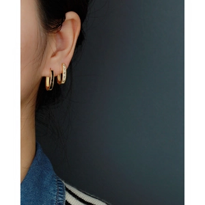 Close-up of gold hoop earrings with black enamel and clear crystals on a model's ear