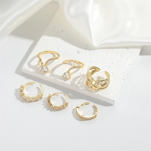 Artistic arrangement of six gold zircon rings and hoops on a textured marble plate