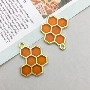 Close-up of two golden honeycomb charms with amber enamel for jewelry making