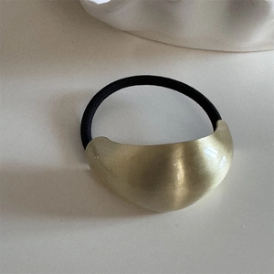 Detail of matte gold irregular metal charm on a black high-elasticity hair tie band