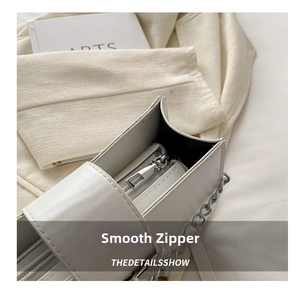 Detail of a smooth silver zipper on a minimalist white leather crossbody bag with chain