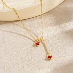 Minimalist gold Y-shaped necklace with elegant red heart pendants on textured stone surface