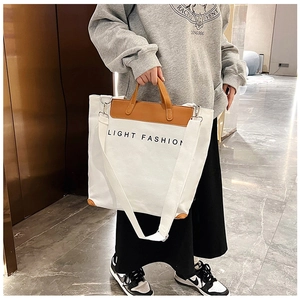 Detail of white canvas tote with brown leather handles and 'LIGHT FASHION' lettering