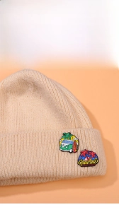 Close-up of summer coconut tree and surf van badges on ribbed cream knit beanie