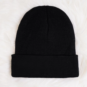 Flat lay of a black knit beanie on a white faux fur background for winter warmth