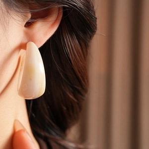 Macro view of C-shaped milky white resin earring on model showing smooth texture