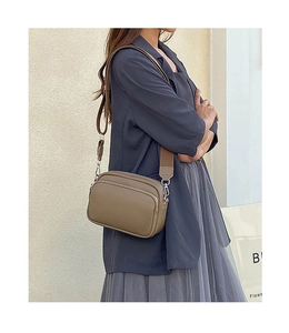 Side view of a brown leather crossbody camera bag with wide strap on a female model