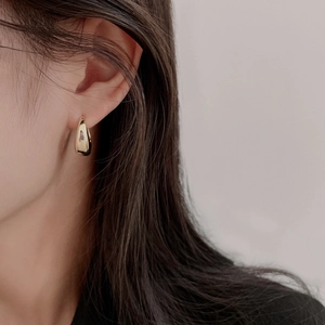 Close-up of a minimalist golden water drop hoop earring on a model's ear with polished finish