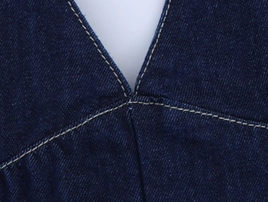 Détail de la couture en V sur une robe en jean bleu foncé avec texture de tissu