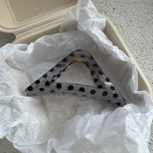 Close-up of a transparent grey triangle hair claw clip with black polka dots in a box