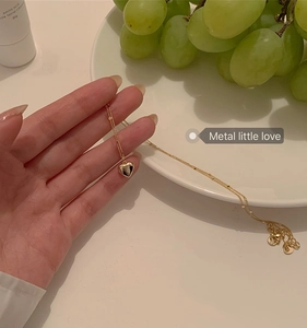 Detailed view of a gold heart pendant necklace held by hand against a lifestyle backdrop